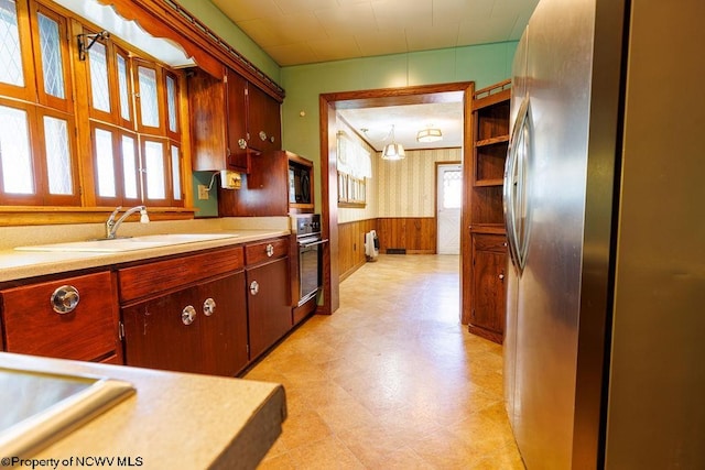 kitchen with wooden walls, oven, black microwave, sink, and stainless steel fridge