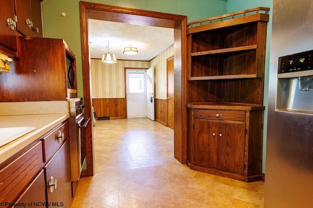 kitchen with a textured ceiling, wood walls, and stainless steel fridge with ice dispenser