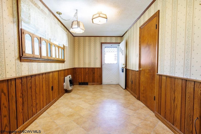 spare room featuring a textured ceiling, ornamental molding, wooden walls, and heating unit