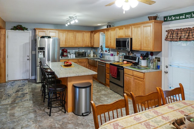 kitchen featuring stainless steel appliances, a center island, light stone countertops, ceiling fan, and a breakfast bar