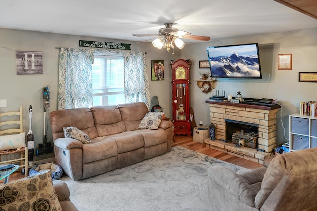 living room featuring light wood-type flooring, ceiling fan, and a stone fireplace