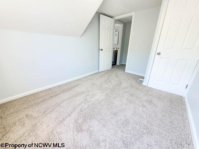 unfurnished bedroom with carpet flooring, baseboards, and vaulted ceiling