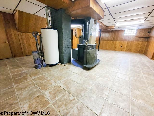 below grade area with wooden walls, heating unit, a wood stove, a drop ceiling, and gas water heater