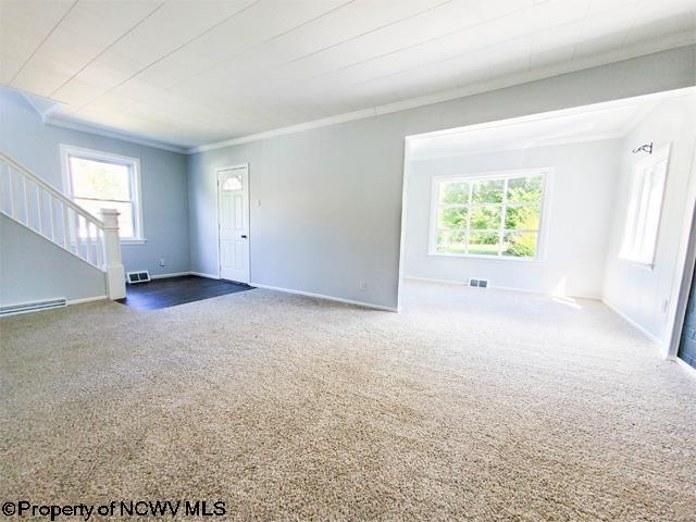 unfurnished living room featuring visible vents, stairway, crown molding, carpet flooring, and baseboards