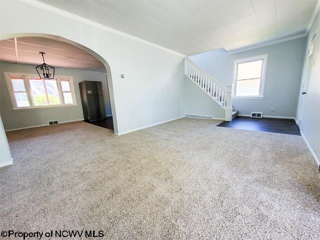 unfurnished living room with an inviting chandelier, crown molding, and carpet floors