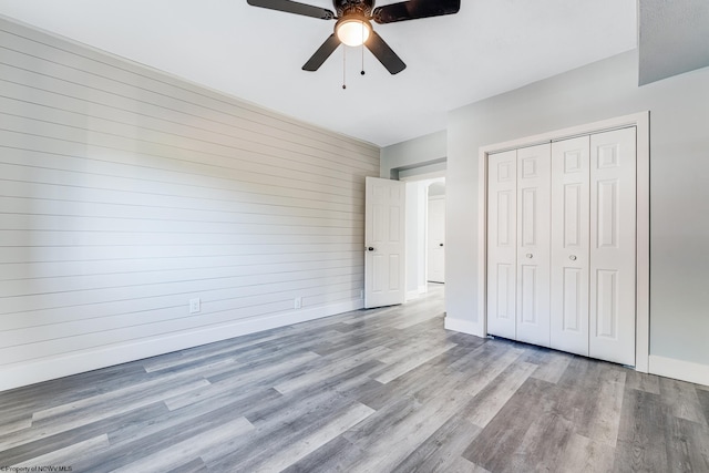 unfurnished bedroom featuring light wood-type flooring, wood walls, ceiling fan, and a closet