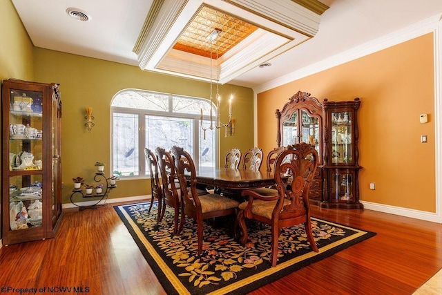 dining room with baseboards, wood finished floors, visible vents, and ornamental molding