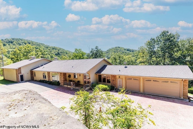 single story home with stucco siding, an attached garage, a wooded view, and driveway