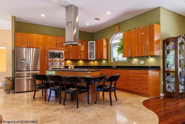 kitchen with brown cabinets, a sink, dark countertops, appliances with stainless steel finishes, and island range hood