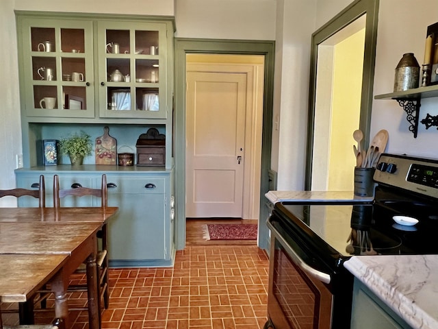 kitchen with green cabinetry, electric range, glass insert cabinets, and brick floor