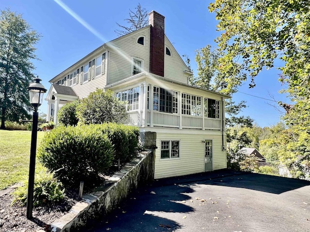 rear view of house featuring a yard, a chimney, and a sunroom