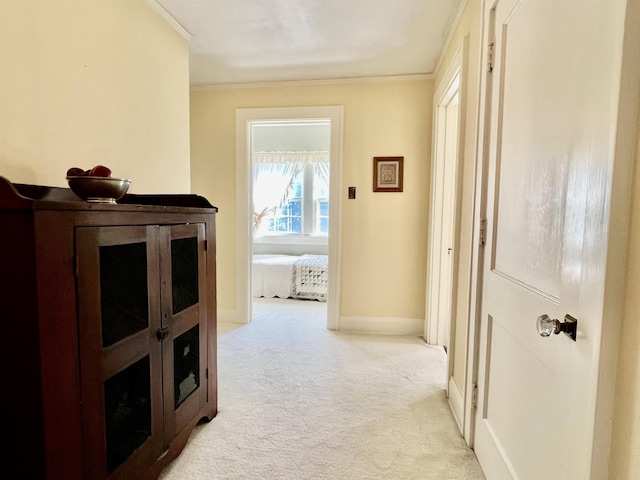 corridor featuring light carpet, baseboards, and ornamental molding