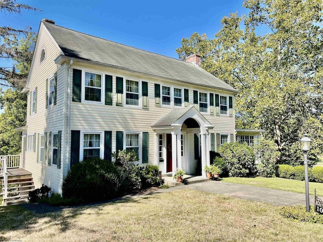 colonial home featuring driveway, a chimney, and a front yard