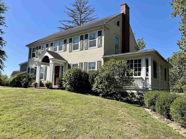 colonial inspired home featuring a front yard, a chimney, and a sunroom