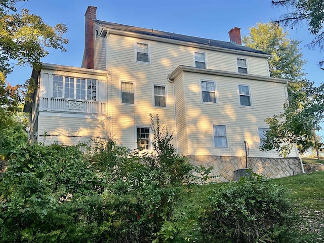 view of side of home with stone siding, a balcony, and a chimney