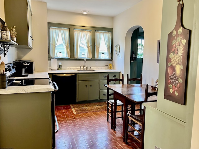 kitchen featuring arched walkways, a sink, light countertops, black dishwasher, and brick patterned floor