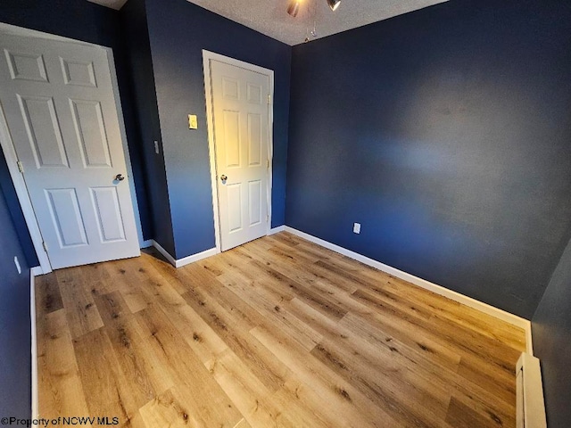 unfurnished bedroom featuring hardwood / wood-style floors, a baseboard heating unit, and a textured ceiling