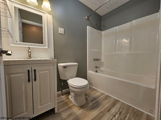 full bathroom featuring washtub / shower combination, vanity, wood-type flooring, toilet, and a textured ceiling