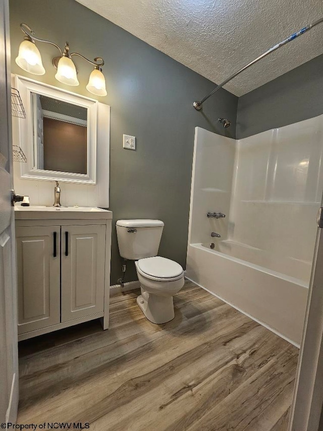 full bathroom featuring vanity, wood-type flooring, a textured ceiling, washtub / shower combination, and toilet