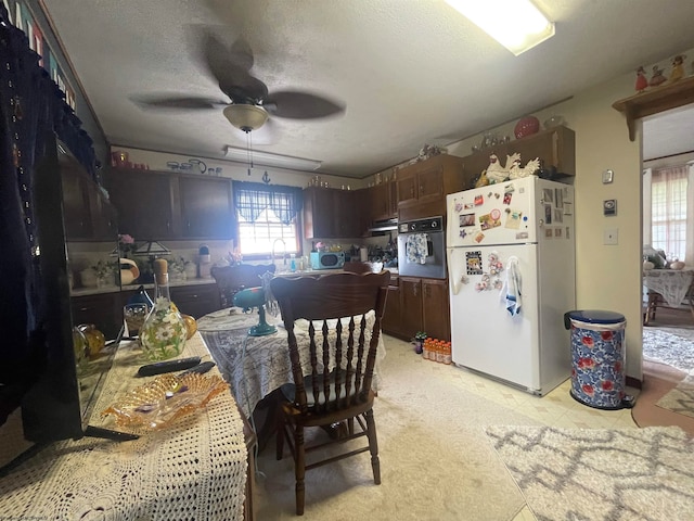 kitchen with dark brown cabinetry, ceiling fan, white refrigerator, a textured ceiling, and black oven