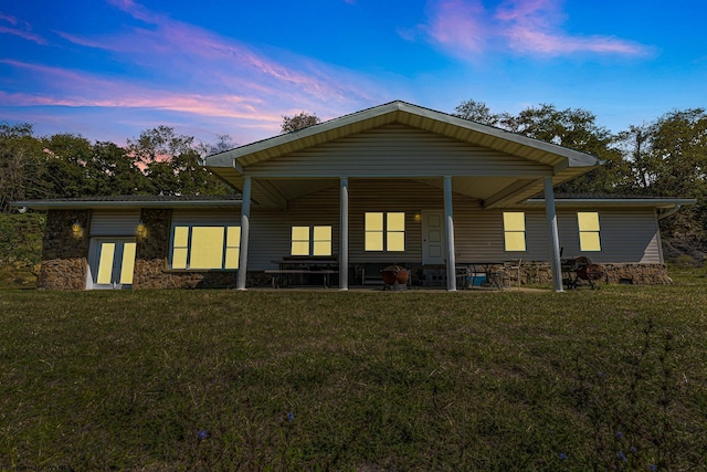 back house at dusk featuring a lawn and a porch