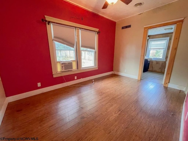 empty room featuring ceiling fan, cooling unit, hardwood / wood-style flooring, and a healthy amount of sunlight