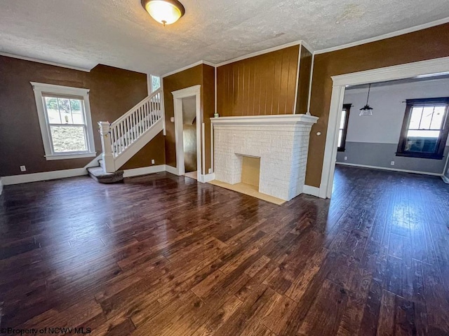 unfurnished living room featuring ornamental molding, a brick fireplace, a textured ceiling, and dark wood-type flooring