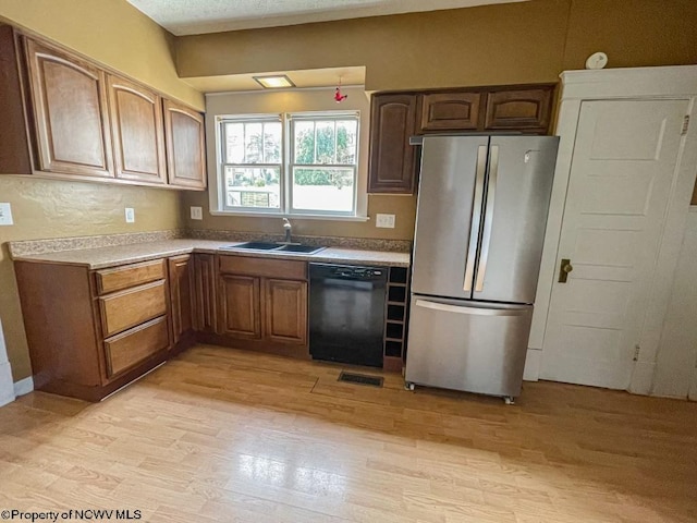 kitchen with stainless steel refrigerator, black dishwasher, a textured ceiling, light hardwood / wood-style flooring, and sink