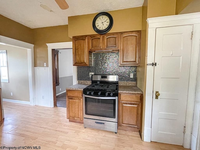 kitchen with a textured ceiling, tasteful backsplash, stainless steel gas range oven, light hardwood / wood-style flooring, and ceiling fan