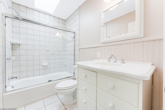bathroom with tile patterned flooring, a wainscoted wall, toilet, and shower / bath combination with glass door