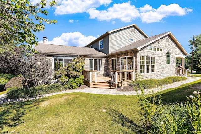 back of house featuring stone siding, a shingled roof, a yard, and a deck