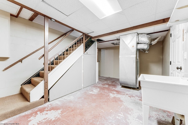finished below grade area featuring stairway, concrete block wall, a paneled ceiling, and a sink