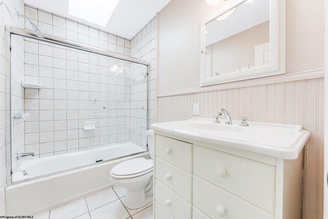 full bathroom with vanity, combined bath / shower with glass door, a skylight, toilet, and tile patterned floors