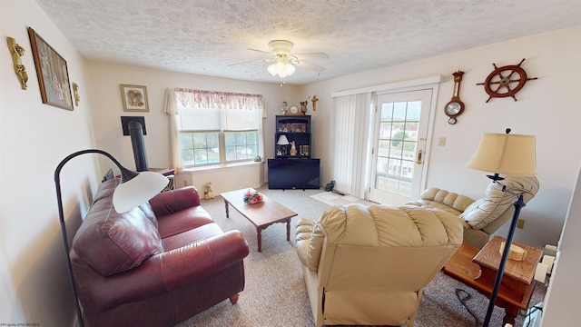 carpeted living room with ceiling fan, a textured ceiling, and a wood stove