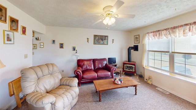 living room featuring a wood stove, ceiling fan, carpet flooring, and a textured ceiling