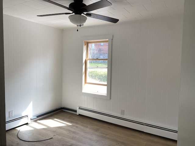 unfurnished room with hardwood / wood-style flooring, wooden walls, a baseboard radiator, and ceiling fan