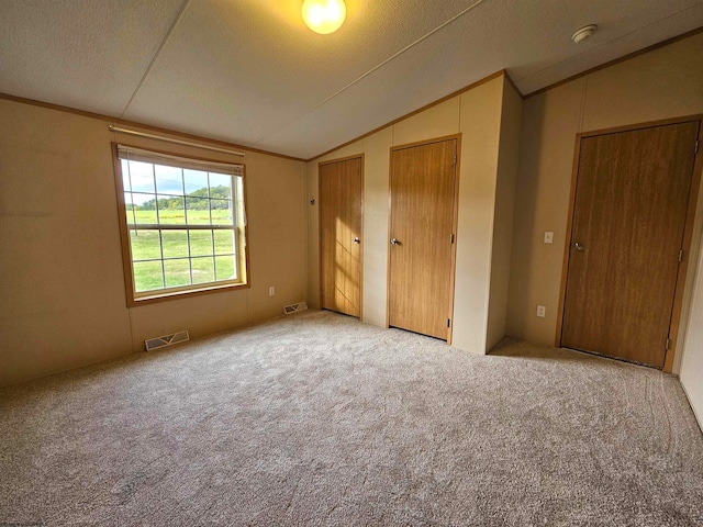 unfurnished bedroom with light carpet, a textured ceiling, lofted ceiling, and two closets