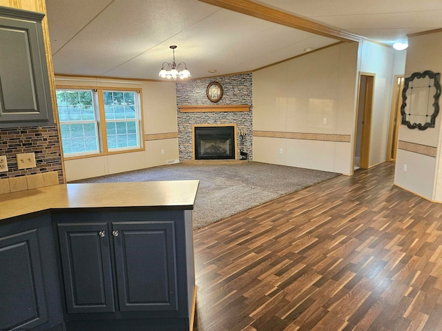 kitchen with pendant lighting, kitchen peninsula, a stone fireplace, an inviting chandelier, and dark hardwood / wood-style flooring