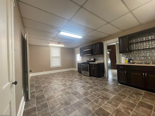 interior space featuring sink, appliances with stainless steel finishes, backsplash, and a drop ceiling