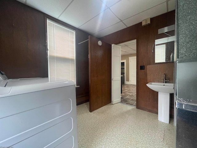 bathroom with a paneled ceiling, wood walls, and washer / dryer