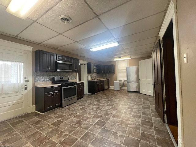 kitchen with appliances with stainless steel finishes, decorative backsplash, and a drop ceiling