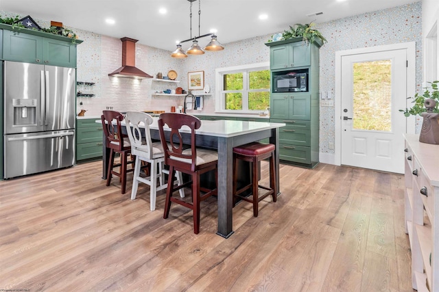 kitchen with pendant lighting, light hardwood / wood-style floors, stainless steel fridge with ice dispenser, wall chimney range hood, and black microwave