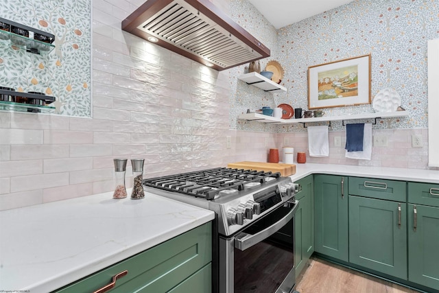 kitchen with wall chimney exhaust hood, stainless steel gas stove, green cabinetry, and tasteful backsplash