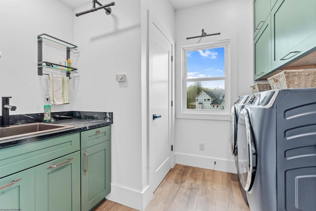 clothes washing area with cabinets, light hardwood / wood-style floors, washer and clothes dryer, and sink