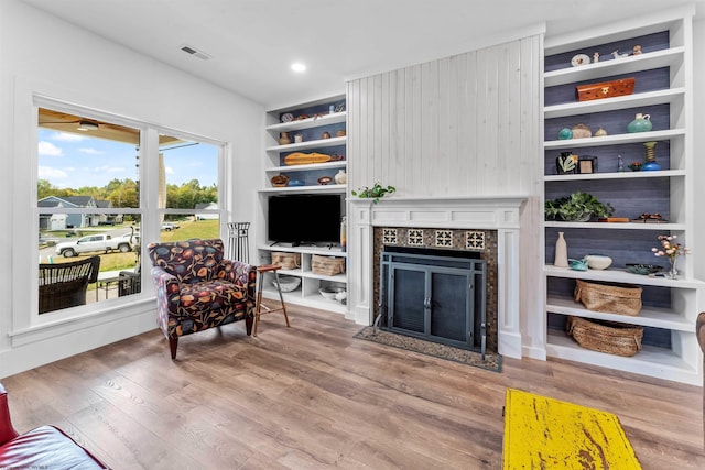 living room with light wood-type flooring, built in shelves, and a tiled fireplace