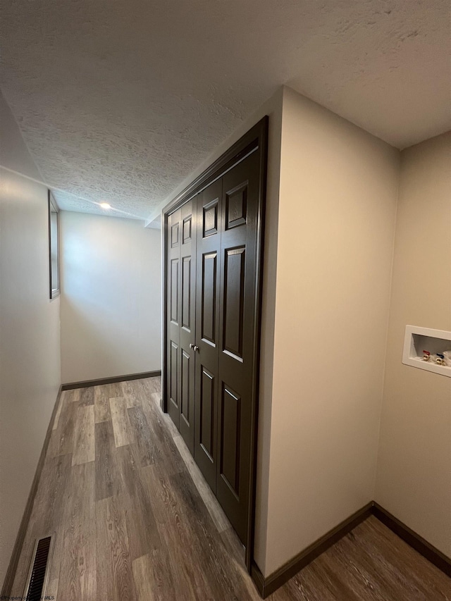 hallway with baseboards, visible vents, a textured ceiling, and wood finished floors