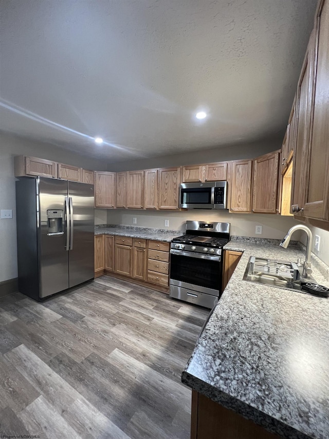 kitchen with dark wood-style floors, appliances with stainless steel finishes, brown cabinets, and a sink