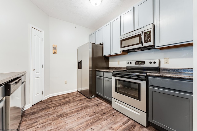 kitchen with a textured ceiling, appliances with stainless steel finishes, dark hardwood / wood-style floors, and gray cabinetry