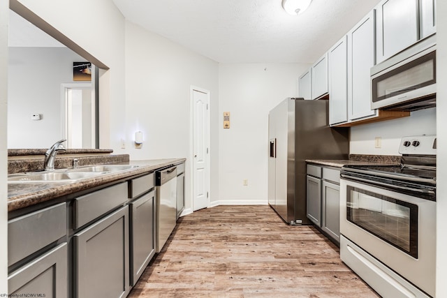 kitchen with light hardwood / wood-style floors, a textured ceiling, sink, gray cabinetry, and stainless steel appliances