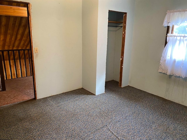 unfurnished bedroom with carpet, wooden walls, and a closet